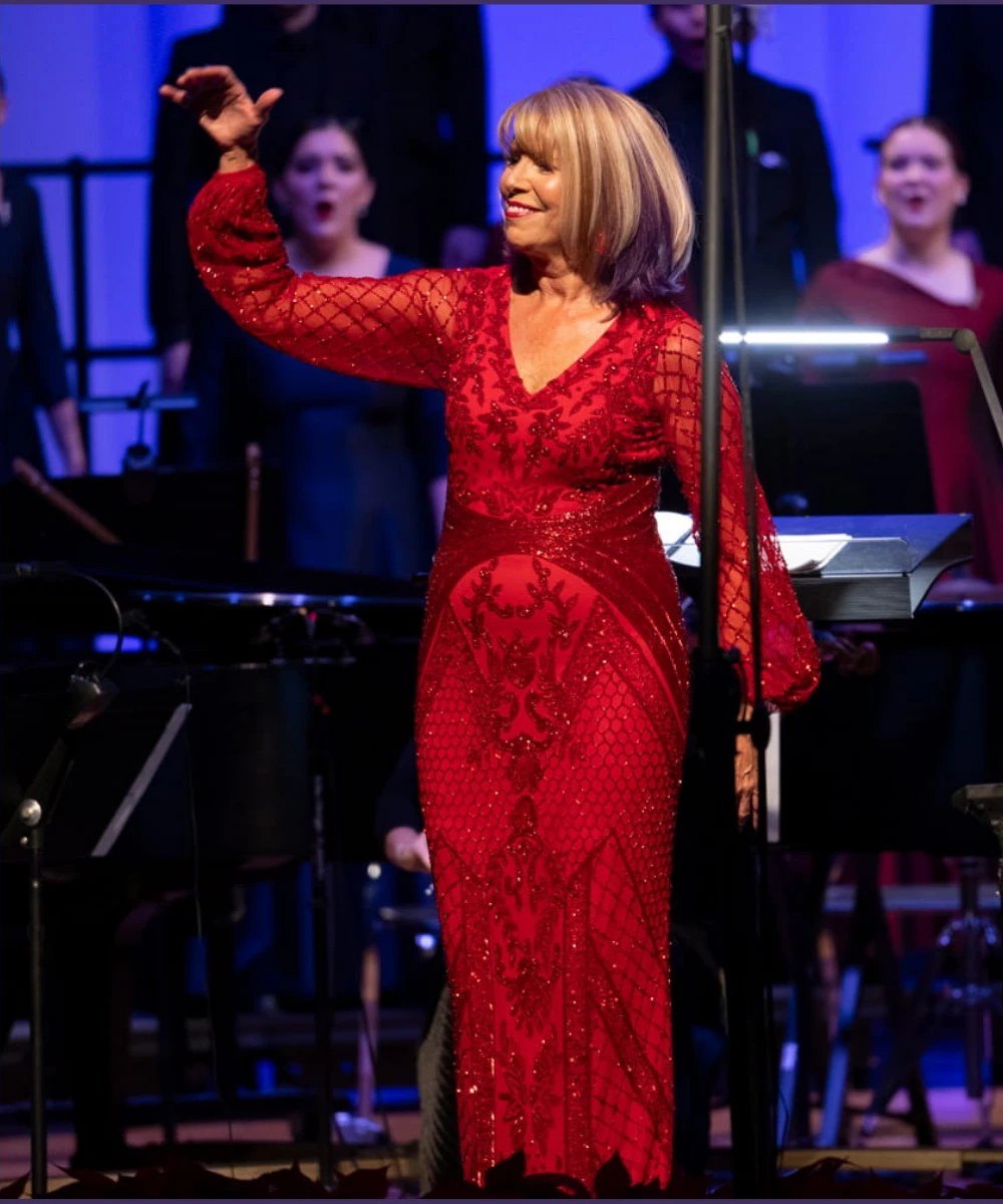 Lynda Hasseler conducting in a red gown, with the choir singing behind her